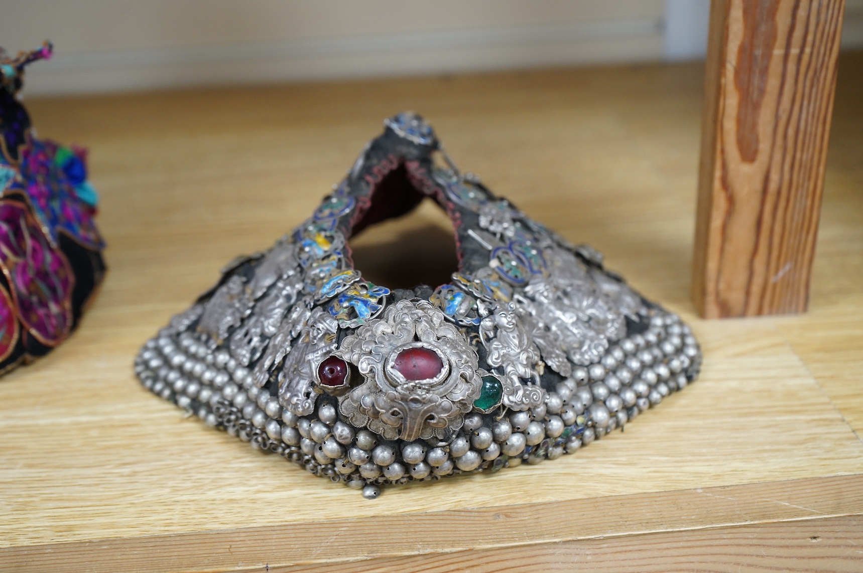 A Chinese Zhuang silver and enamel ceremonial hat, Yunnan Province. The hat heavily covered with auspicious silver and silver enamel charms for good luck and prosperity with a tail/horn shape one side and large silver fl